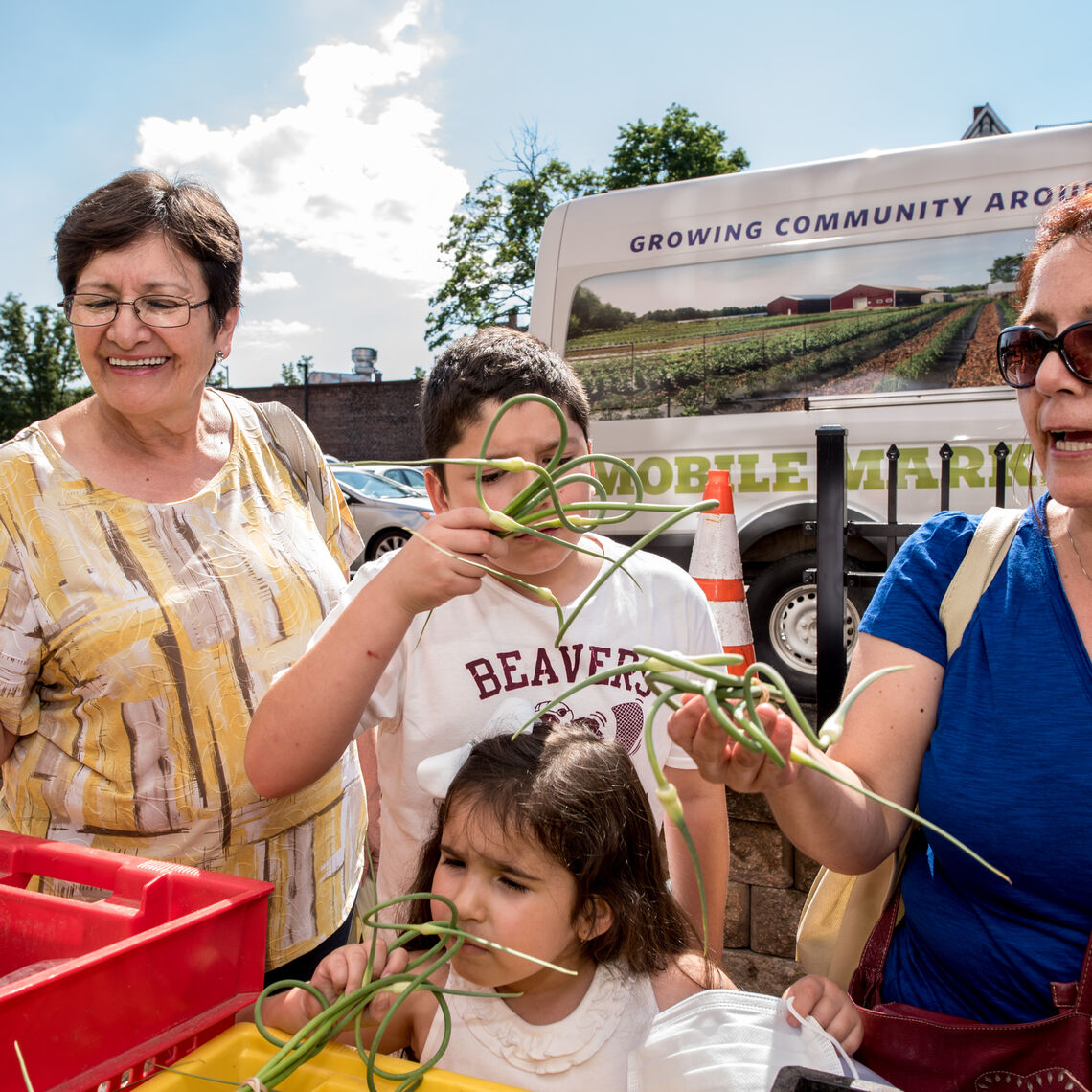A multi-generational family smells garlic scapes at a farm vendor that accepts HIP